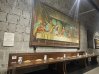 A display inspired by The Last Supper with bread and pitchers set along a long table beneath a mural.